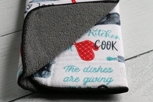 Cute drying dish mat that is reversible, one side is white with cookware, utensils, hearts, and words, the other side is solid gray with a black edging.